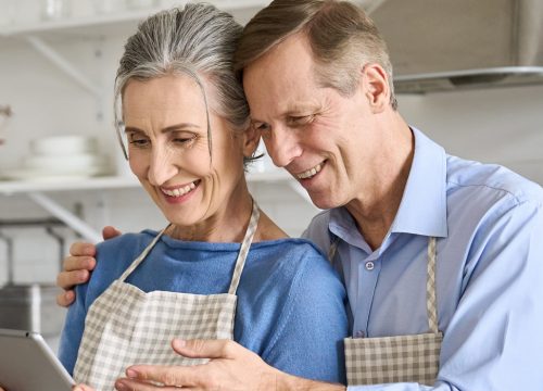 Happy older couple cooking in the kitchen, holding a tablet
