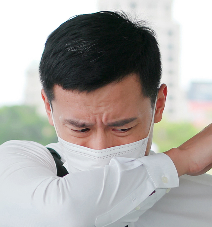 Man wearing a mask, coughing into his arm